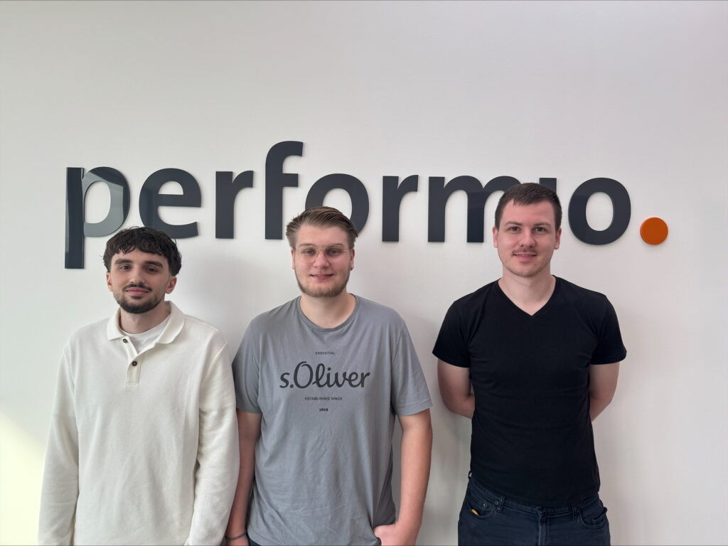 Drei Männer vor dem performio Logo